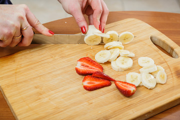 Beautiful female hands cut strawberries in the kitchen
