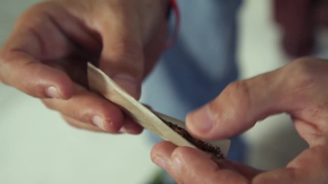 Substance abuse, drugs, narcotics and people, hispanic man preparing hashish joint at home for smoking. Young person using marijuana cigarette as recreational drug