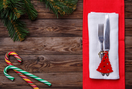 Christmas table place setting with fork and knife, decorated christmas toy - red fir-tree, two lollipop cane and christmas pine branches.