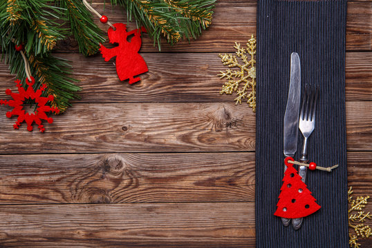 Christmas table place setting with fork and knife, decorated christmas toy - red fir-tree, gold snowflakes and christmas pine branches.