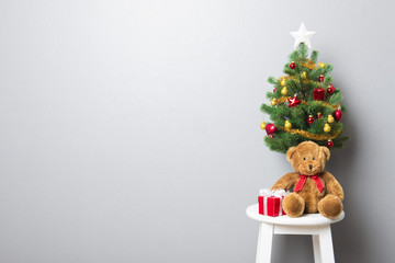 Gift boxes, teddy bear and small decorated Christmas tree on stool