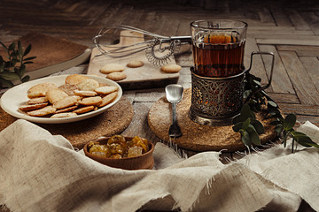 Hot tea in antique cup holder with sugar cookies on old brown wooden background. Rustic style. Breakfast background.