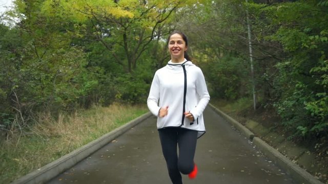 A young fit healthy woman jogging and smiling in the park slow motion