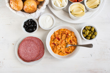 Traditional Turkish breakfast, top view: cooked egg menemen, pogaca pasties, vegetables, cheeses, olives and halal turkey salami, selective focus