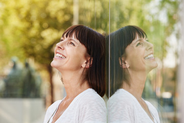 Smiling friendly woman leaning against reflection in building