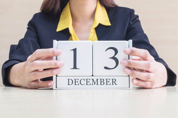 Closeup white wooden calendar with black 13 december word in blurred working woman hand on wood desk in office room , selective focus at the calendar