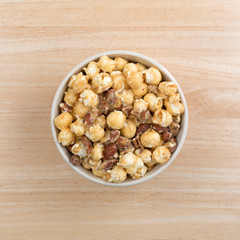 Gourmet popcorn with nuts in a bowl top view atop a wood table.