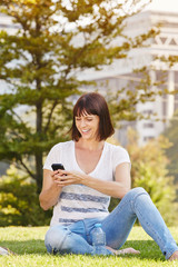 Happy woman sitting in grass with water with cellphone