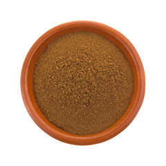 Carob powder in a bowl top view isolated on a white background.
