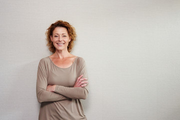 Older woman smiling with arms crossed by wall