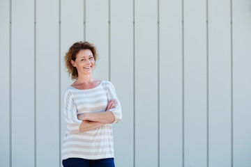 Cheerful woman standing by wall with arms crossed