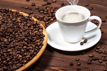 A cup of coffee on a wooden table. Coffee beans in a large dish.