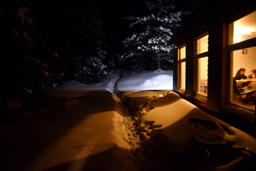 Chimney light of a cottage illuminate the snow outside at winter