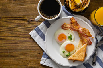Fototapeta na wymiar American breakfast with sunny side up eggs, bacon, toast, pancakes, coffee and juice