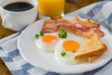 American breakfast with sunny side up eggs, bacon, toast, pancakes, coffee and juice