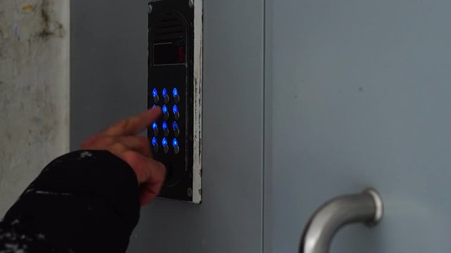 Male hand dials a code of intercome and opens a door of a house