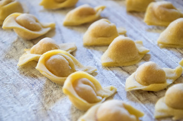  Raw italian cappelletti, fresh homemade pasta stuffed with cheese and meat on rustic wood table. Natural light.