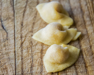  Raw italian cappelletti, fresh homemade pasta stuffed with cheese and meat on rustic wood table. Natural light.