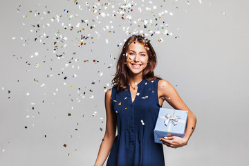 Beautiful happy woman with gift box at celebration party with confetti falling everywhere on her....