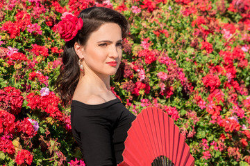 Young beautiful woman in a flamenco costume.  Red flowers on the background. 