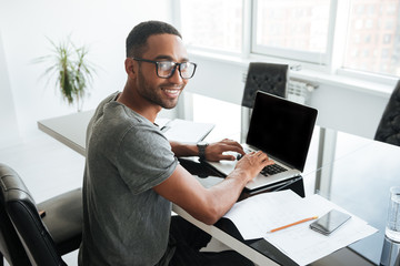 Cheerful african man using laptop and looking at the camera