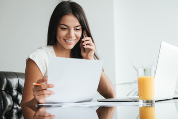 Young lady analyzing home finances while talking by phone