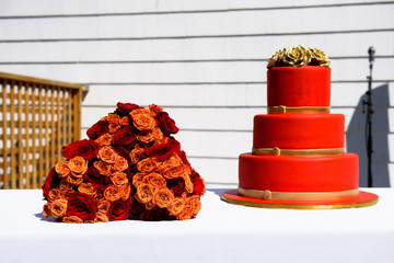 Red bouquet lies behind red wedding cake with golden roses on to