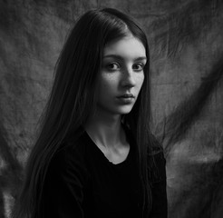 Dramatic black and white portrait of a beautiful lonely girl with freckles isolated on a dark background in studio shot