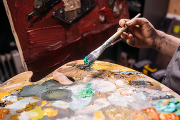 Artist holds a palette and a brush, paints a picture. Creative process of drawing in workroom....