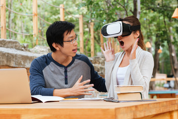 Surprised woman sitting with friend and using virtual reality glasses