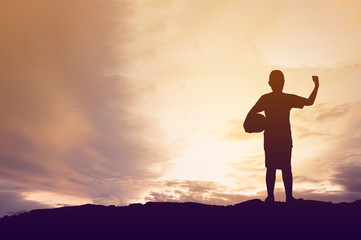 Obraz premium Silhouette little boy holding football on sun sky background.