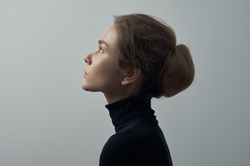 Dramatic portrait of a young beautiful girl with freckles in a black turtleneck on white background in studio