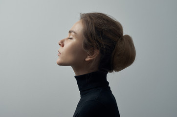 Obraz premium Dramatic portrait of a young beautiful girl with freckles in a black turtleneck on white background in studio