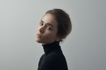 Dramatic portrait of a young beautiful girl with freckles in a black turtleneck on white background in studio - 129438595