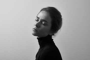 Dramatic black and white portrait of young beautiful girl with freckles in a black turtleneck on white background in studio