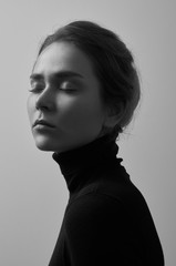 Dramatic black and white portrait of young beautiful girl with freckles in a black turtleneck on white background in studio
