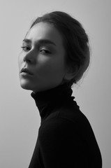 Dramatic black and white portrait of young beautiful girl with freckles in a black turtleneck on white background in studio