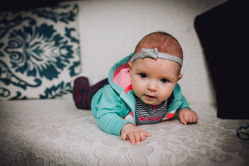 Fototapeta premium Baby girl plays on the couch at home. Baby newborn attentively looks.