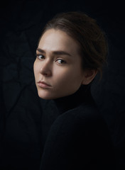 Dramatic portrait of a young beautiful girl with freckles in a black turtleneck on black background in studio - 129439119