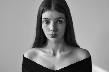 Dramatic black and white portrait of a beautiful lonely girl with freckles isolated on a white background in studio shot