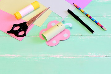 Naklejka premium Funny paper butterfly crafts, scissors, marker, glue stick, pencil, colored paper, pencil on green wooden background with blank place for text. Kids summer diy in kindergarten or at home
