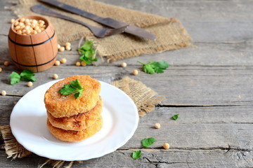 Fried pea cutlets on a plate. Healthy vegan cutlets cooked from yellow dried peas and decorated with parsley. Fork, knife on an old wooden background with copy space for text. Vegan food idea. Closeup