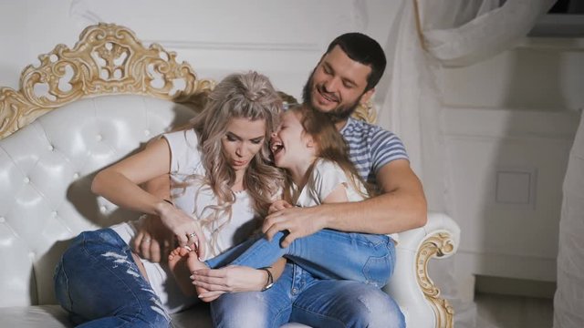 Close-up of happy family expecting new baby playing together on the sofa. Father, pregnant mother and little daughter are sitting together on the sofa hugging each other and smiling.