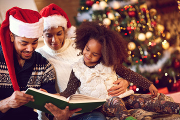 mother, father and daughter read a book at fireplace on Christma