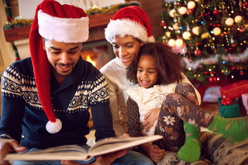 Fototapeta na wymiar Happy afro American family read a book at fireplace on Christmas