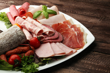 Food tray with delicious salami, pieces of sliced ham, sausage, tomatoes, salad and vegetable - Meat platter with selection