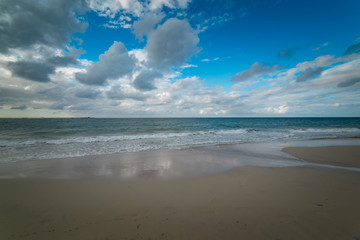 The Indian Ocean laps gently onto the white sandy shore of beautiful beach near Busselton, South Western Australia protected by Geographe Bay on a  blue sky and white cloud afternoon in early summer.