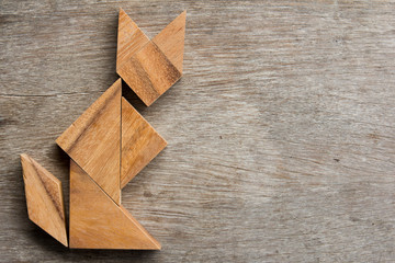 Wooden tangram as cat sitting shape on old wood background