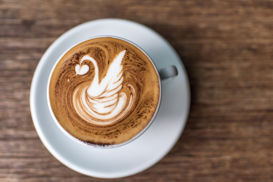 
a cup of coffee with latte art in a swan shape on a wooden table