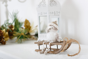 Xmas or new year composition with holiday decoration - lamp and little owl figure sitting on sledge on white background. Xmas card